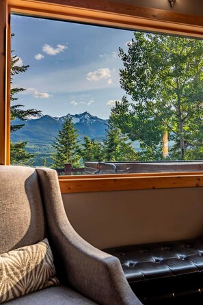 A room with a view of a mountain range through a window, a leather sofa, and a wooden bench. - Mountain Escape. Sauna & Soak. (Columbia-Shuswap)