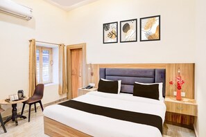 A hotel room with a bed, bedside table, chair, window, and artwork on the wall. - Hotel O Tyagi Road Near Railway Station (Dehradun)