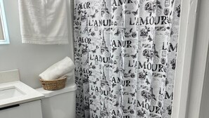 Une salle de bain comprenant des toilettes, un lavabo blanc, une serviette blanche, un tapis de bain noir et un rideau de douche à motifs.