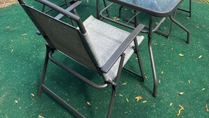 Une terrasse dotée d’une table à plateau en verre et de quatre chaises, le tout entouré d’une clôture en bois.