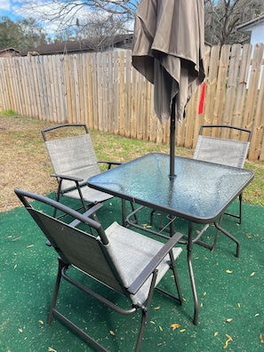 Un patio con una mesa de vidrio y cuatro sillas, rodeado por una valla de madera.