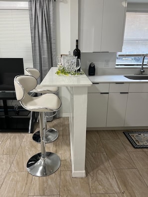 Una cocina moderna con una isla central, taburetes de bar, una botella de vino y un fregadero.