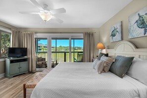 A bedroom with a bed, a television, a ceiling fan, and a view of a balcony with a pool. - Seascape 3 BD/2 BA condo- 3 min walk to beach! Miramar Beach Destin (Miramar Beach)