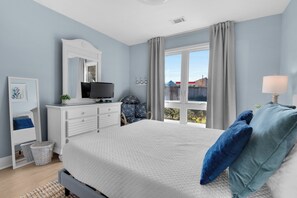 Ein Schlafzimmer mit Bett, Kommode, Fernseher und einem Fenster mit Vorhängen.