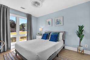 A bedroom with a large bed, a bedside table with a lamp, a potted plant, and artwork on the wall. - Seascape 3 BD/2 BA condo- 3 min walk to beach! Miramar Beach Destin (Miramar Beach)