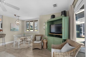 Ein Wohnzimmer mit Fernseher, Korbmöbeln, einem Esstisch und einem Deckenventilator.