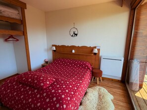 Ein Schlafzimmer mit einem hölzernen Kopfende, einer roten blumigen Tagesdecke, einem kleinen Nachttisch mit Lampe und einem Fenster mit Blick.