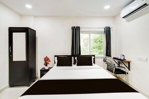 A hotel room with a bed, a desk, a chair, a wardrobe, and an air conditioning unit. - Townhouse Near Narsingi Manikonda (Hyderabad)