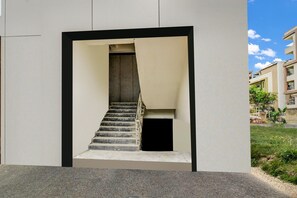 A modern building with a central staircase, a small enclosed area at the bottom, and a clear sky. - Townhouse Near Narsingi Manikonda (Hyderabad)