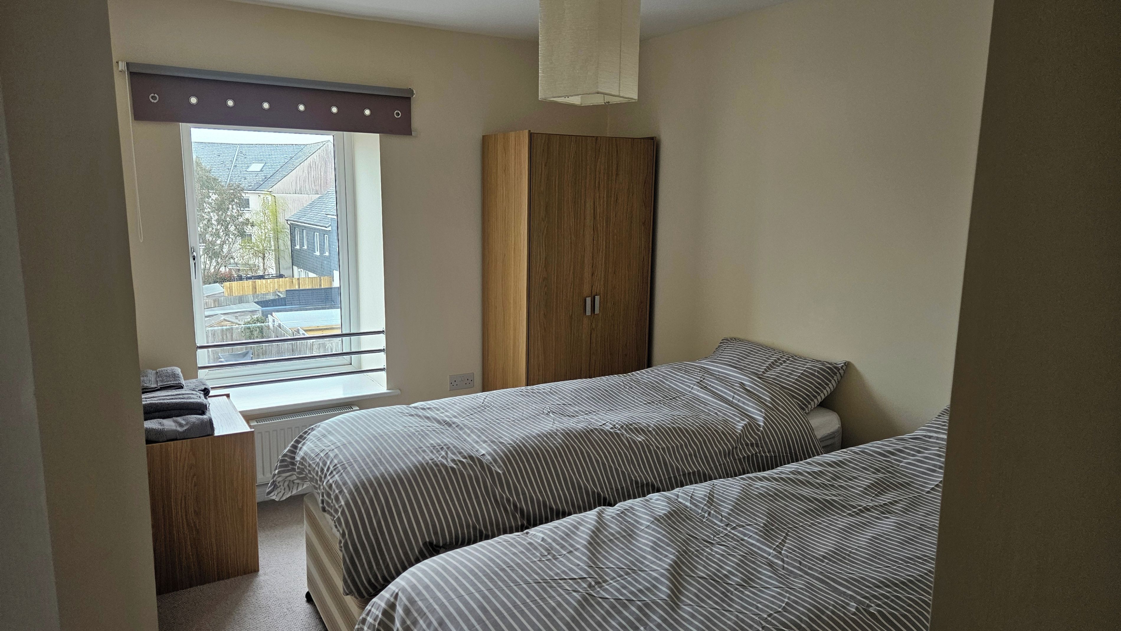 A bedroom with two beds, a window with a view of buildings, and a wooden wardrobe.
