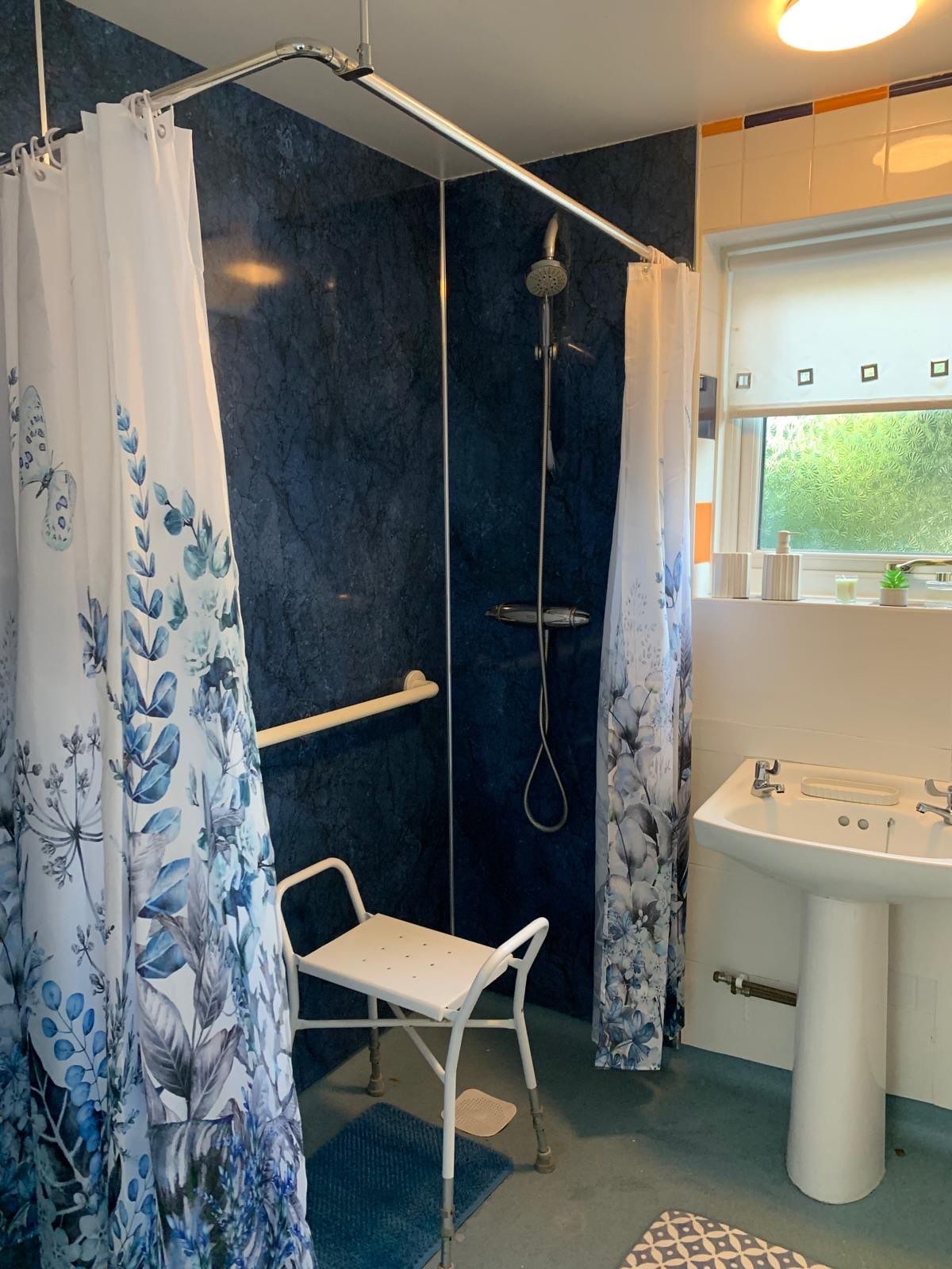 A bathroom with a shower, a sink, and a chair.