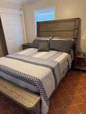 Un dormitorio con cama, mesita de noche, lámpara y ventana con persianas.