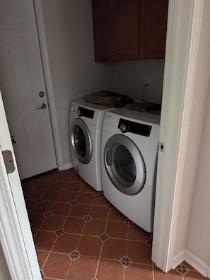Un lavadero con dos lavadoras de carga frontal, una puerta y piso de baldosas.