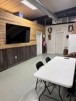 A conference room with a large table, chairs, a TV mounted on the wall, and a door leading to another room.