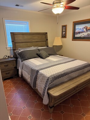 Ein Schlafzimmer mit Bett, Nachttisch, Lampe, Deckenventilator und einem Fenster mit Jalousien.