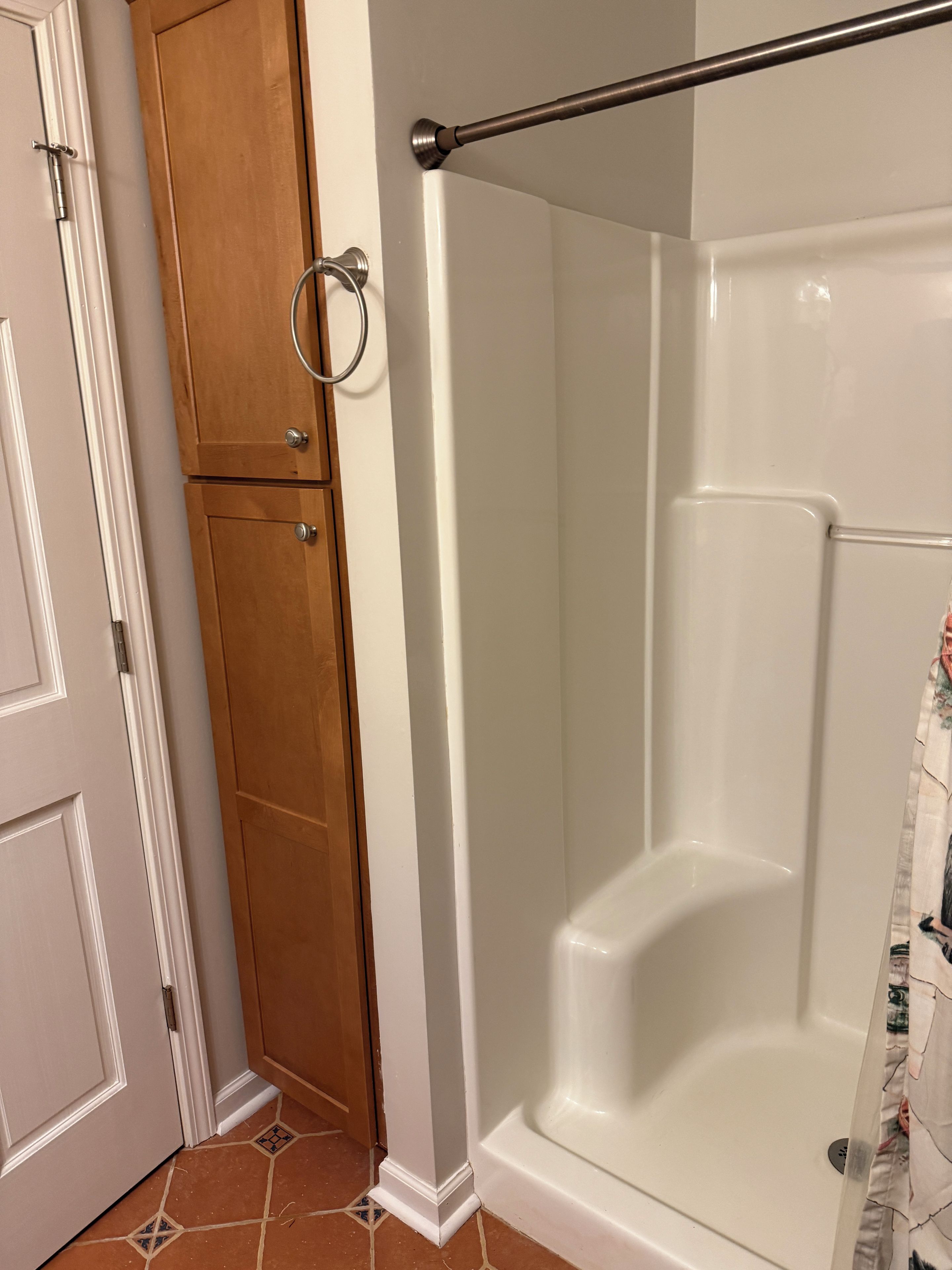 A bathroom with a shower, a wooden cabinet, and a tiled floor.