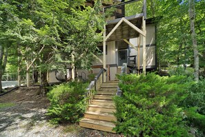 A wooden staircase leading to a building with a sloped roof, surrounded by lush greenery and trees. - Beech Mountain Cabin with Retro Mountain Charm (Beech Mountain)