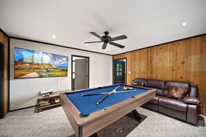 A room with a pool table, a leather sofa, a ceiling fan, and a large landscape painting. - Beech Mountain Cabin with Retro Mountain Charm (Beech Mountain)
