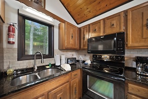 A kitchen with wooden cabinets, a stainless steel sink, a microwave, and an oven. - Beech Mountain Cabin with Retro Mountain Charm (Beech Mountain)