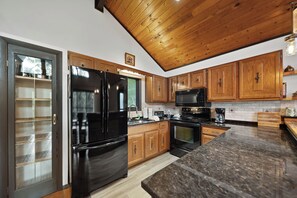 A modern kitchen with a black refrigerator, wooden cabinets, a microwave, and a stove. - Beech Mountain Cabin with Retro Mountain Charm (Beech Mountain)