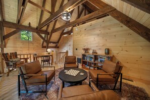 Ein gemütliches Cabin-Interieur mit hoher Decke, Holzbalken, einem Essbereich und einem Bücherregal.