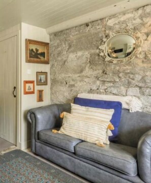 Habitació amb paret de pedra, un sofà de cuir gris i un mirall.