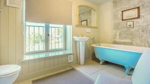 Ein Badezimmer mit Fenster, Waschbecken, Toilette und einer blauen Badewanne.