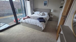 Ein Hotelzimmer mit Bett, Nachttisch, Lampe und Blick auf die Straße durch ein großes Fenster.