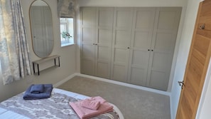 A bedroom with a bed, a wardrobe, a mirror, and a window with curtains. - Stunning Plymouth Harbour Views|Close to Historic Barbican|3 Bedroom House of Stylish Design (Plymouth)