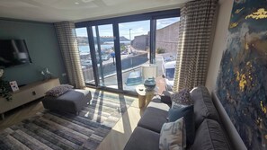 A modern living room with a large window, a flat-screen TV, a sofa, and a coffee table. - Stunning Plymouth Harbour Views|Close to Historic Barbican|3 Bedroom House of Stylish Design (Plymouth)