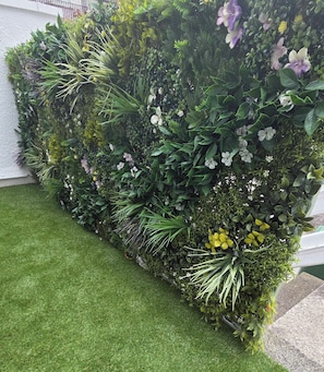 A vertical garden with a variety of plants and flowers, a grassy area in front, and a white wall in the background. - Stunning Plymouth Harbour Views|Close to Historic Barbican|3 Bedroom House of Stylish Design (Plymouth)