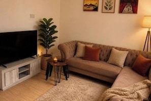 Een woonkamer met een flatscreen televisie, een bank, een salontafel, een potplant en een lamp.