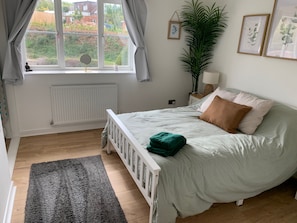 Ein Schlafzimmer mit einem Bett, einem Heizkörper, einem Fenster mit Vorhängen, einer Pflanze und gerahmten Bildern an der Wand.