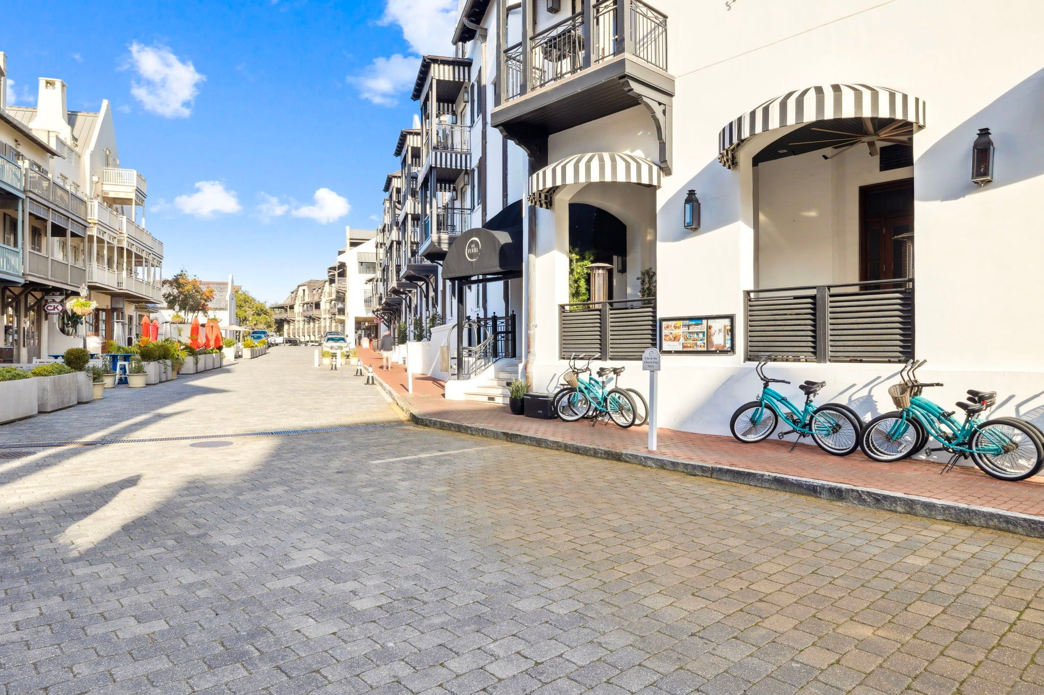 A cobblestone street lined with multi-story buildings, bicycles parked on the sidewalk, and a clear blue sky.