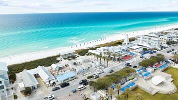 An aerial view of a coastal area with a beach, buildings, and a parking lot.