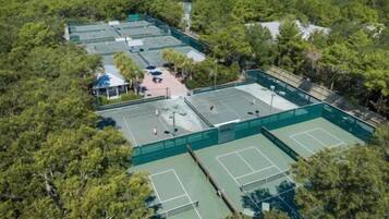 An aerial view of a tennis court complex surrounded by dense forest.