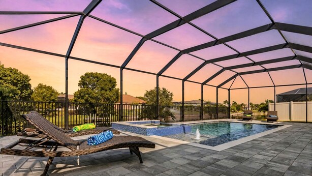 An outdoor swimming pool with a covered area, lounge chairs, and a view of the surrounding landscape. - Your Waterfront Escape | Pool, Spa & Firelight (Cape Coral)