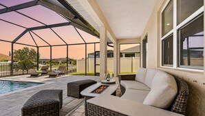 A covered outdoor patio with a pool, wicker furniture, and a fire feature. - Your Waterfront Escape | Pool, Spa & Firelight (Cape Coral)