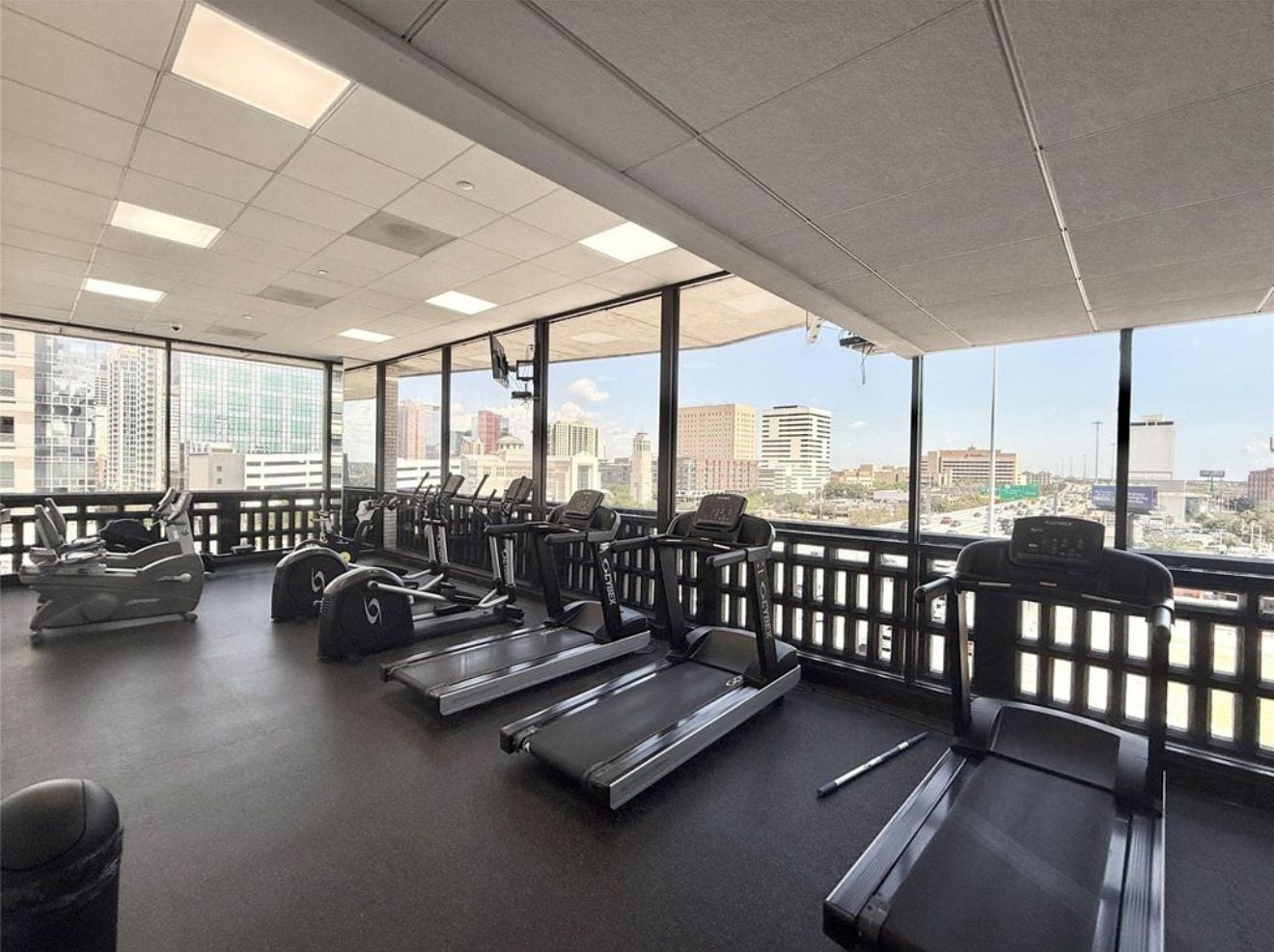 A gym with treadmills, stationary bikes, and a rowing machine, with large windows offering a city view.