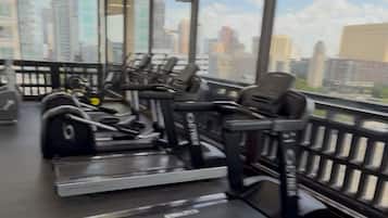 Et fitnesscenter med løbebånd og træningsudstyr, store vinduer med udsigt over byen og et loft med indbygningsbelysning.