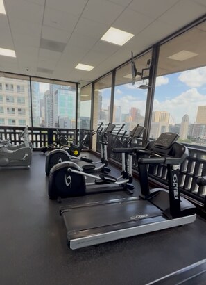 A gym with treadmills and weight machines, large windows with a city view, and a ceiling with recessed lighting.