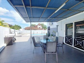 An outdoor patio with a covered seating area, a pool in the background, and a white building with a garage. - Melaka A’Famosa Grand Pool Villa – Private Pool & Family Getaway (Alor Gajah)
