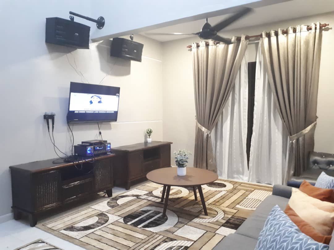 Un salon comprenant un téléviseur, un ventilateur de plafond, un meuble en bois foncé, une table basse ronde et un tapis à motifs.