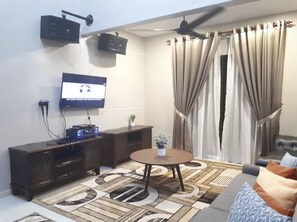 A living room with a television, a ceiling fan, a dark wooden cabinet, a round coffee table, and a patterned rug.