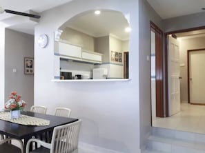 A dining area with a table and chairs, a clock on the wall, and a kitchen visible through an archway.