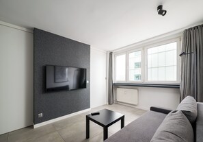 A modern living room with a flat-screen TV mounted on a textured wall, a black coffee table, a grey sofa, and a large window with curtains. - City Center Śliska Apartment (Warszawa)