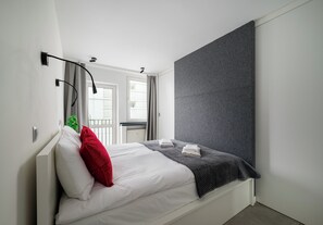 A modern hotel room with a bed, a grey textured wall, and a window with curtains. - City Center Śliska Apartment (Warszawa)