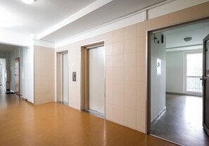 A corridor with doors leading to individual rooms, a visible elevator, and a window at the end of the corridor. - City Center Śliska Apartment (Warszawa)