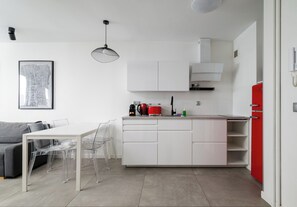 Una cocina moderna con armarios blancos, una mesa de comedor con sillas transparentes y un electrodoméstico rojo.