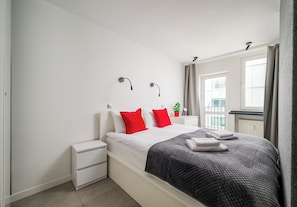 A modern bedroom with a bed, white nightstands, a bedside table, a window with curtains, and a view of the outside. - City Center Śliska Apartment (Warszawa)